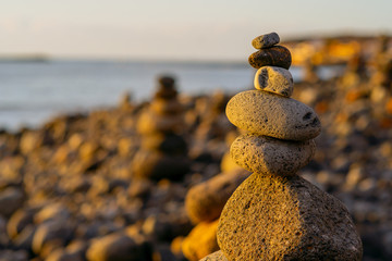 Balanced stone pyramide on shore of the ocean at dawn. Sea pebbles tower closeup symbolizing stability, zen, harmony, balance.