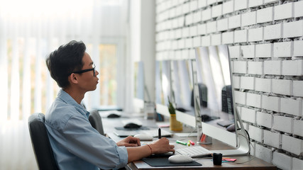 Wall Mural - staying focused at work. side view of a young asian graphic designer in eyeglasses using digital gra