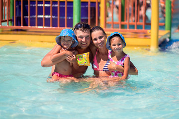 Happy European family with two children swimming in the pool of a large beautiful water park during summer vacation