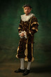 Posing thoughtful. Portrait of medieval young man in vintage clothing standing on dark background. Male model as a duke, prince, royal person. Concept of comparison of eras, modern, fashion.