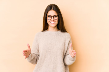 Wall Mural - Young caucasian woman isolated on beige background holding something with both hands, product presentation.