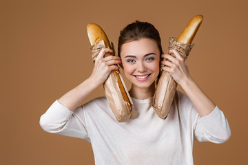 Wall Mural - Portrait of beautiful smiling young woman holding paper bag with bread on studio yellow background. funny girl with paper bag with fresh fragrant long loaf