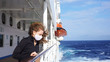 © Artem - Curly girl in a medical respirator on board a cruise ship on a sunny day against the background of the sea. quarantined european girl on promenade deck of cruise ship