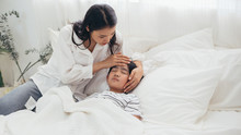 Young Asian Mother Hand Take Care And Checking Her Son Fever Temperature, Sick Boy Sleeping In Bed, Woman Worried Of Corona Influenza, Medical Healthcare And Prevent Epidemic Disease Flu Virus Concept