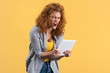 © LIGHTFIELD STUDIOS - angry redhead girl shouting at digital tablet, isolated on yellow