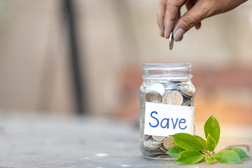 Wall Mural - Hand holding coins putting into glass jar with blur nature background , saving money concept , Billing concept , Investment And Interest Concept