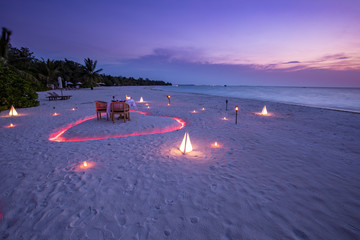 Wall Mural - A young couple share a romantic dinner with candles heart on the sea sand beach