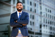 © elnariz - Confident successful african american businessman standing with arms folded, smiling, downtown financial district