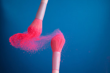 close-up photo of two professional make-up brushes with pink powder in motion on blue background