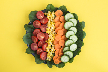 Wall Mural - Chopped vegetables in the black plate in the center of  the yellow  background. Top view. Copy space. Healthy food ingredients.