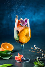 Fresh Tropical Cocktail With Orange, Grapes, Mint, Edible Flowers And Ice In Wine Glass On Dark Blue Background. Summer Cold Drink And Cocktail