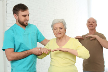 Canvas Print - Care worker helping elderly woman to do sports exercise in hospital gym.