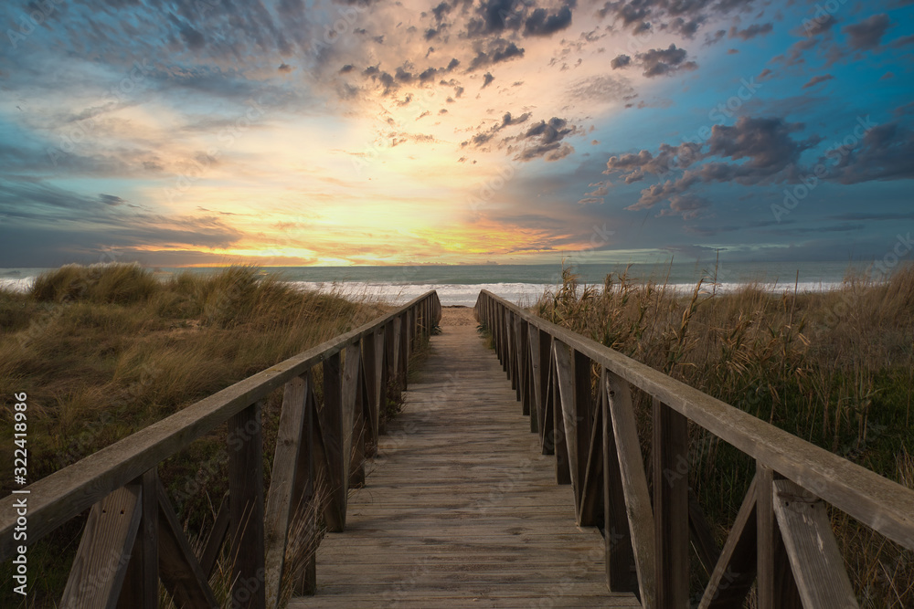 Wooden path and sunset on the beach of El Palmar, near the Caños de Meca, an ideal place to spend a great holiday on the coast of the province of Cadiz, in Andalusia, Spain - obrazy, fototapety, plakaty 