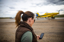 Female Pilot With Smart Phone On Runway With Crop Sprayer