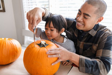 Girl Helping Father Carve Halloween Pumpkin
