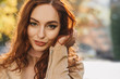 © Look! - Close-up portrait of sensual young woman playing with dark ginger hair. Dreamy red-haired girl posing with smile on blur background.