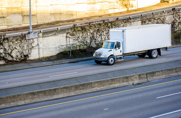 Medium duty semi truck with box trailer transporting commercial cargo running on the divided wide highway road for delivery