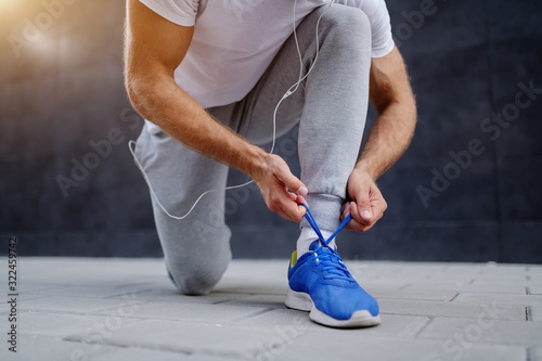Fotomural Close up of caucasian sportsman in tracksuit tying shoelace while kneeling outdoors