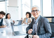 © Sanja - A mature business lady sitting at the table with a laptop in the conference room, looking at the camera. She is smiling, she cares about her work.