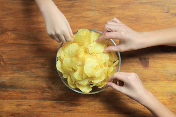 Big family eating potato chips from bowl, top view