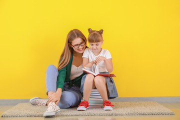 Canvas Print - Cute little girl and her mother reading books near color wall