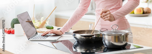 Fotografía Woman cooking lunch according to recipe on laptop