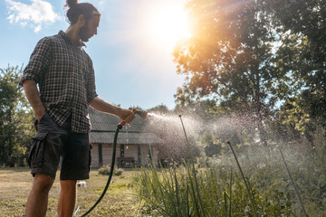 Hipster young man watering plants a country house, summer spring and garden care, organic products, eco-friendly lifestyle