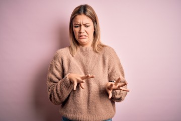 Young beautiful blonde woman wearing winter wool sweater over pink isolated background disgusted expression, displeased and fearful doing disgust face because aversion reaction.