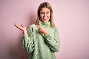 Poster - Young beautiful blonde woman wearing winter wool sweater over pink isolated background amazed and smiling to the camera while presenting with hand and pointing with finger.