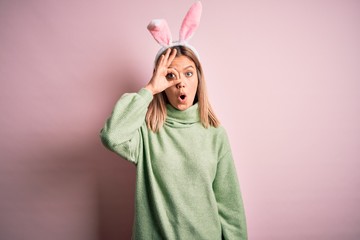 Poster - Young beautiful woman wearing easter rabbit ears standing over isolated pink background doing ok gesture shocked with surprised face, eye looking through fingers. Unbelieving expression.