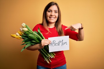 Canvas Print - Beautiful woman holding paper with best mom message and tulips celebrating mothers day with surprise face pointing finger to himself