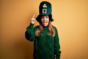 Sticker - Young beautiful brunette woman wearing green hat on st patricks day celebration pointing finger up with successful idea. Exited and happy. Number one.