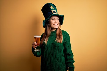 Canvas Print - Young beautiful woman wearing green hat drinking glass of beer on saint patricks day looking away to side with smile on face, natural expression. Laughing confident.