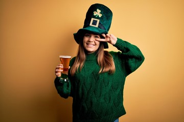 Sticker - Young beautiful woman wearing green hat drinking glass of beer on saint patricks day Doing peace symbol with fingers over face, smiling cheerful showing victory