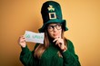 © Krakenimages.com - Young beautiful woman wearing green hat and glasses on saint patricks day celebration serious face thinking about question, very confused idea