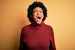 © Krakenimages.com - Young beautiful African American afro woman with curly hair wearing casual turtleneck sweater angry and mad screaming frustrated and furious, shouting with anger. Rage and aggressive concept.