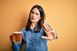 © Krakenimages.com - Young woman with blue eyes drinking jar of beer standing over isolated yellow background doing stop gesture with hands palms, angry and frustration expression