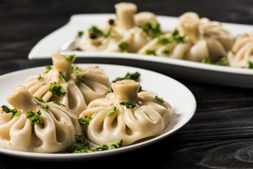 selective focus of delicious Khinkali with cilantro on plates on black wooden table