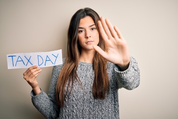 Sticker - Young beautiful girl holding paper with tax day message standing over white background with open hand doing stop sign with serious and confident expression, defense gesture