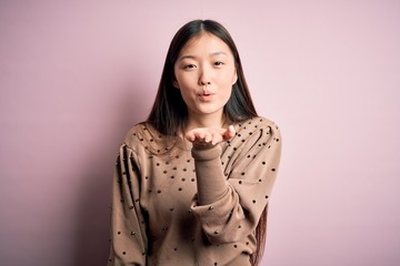 Sticker - Young beautiful asian woman wearing fashion and elegant sweater over pink solated background looking at the camera blowing a kiss with hand on air being lovely and sexy. Love expression.