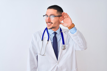 Wall Mural - Young doctor man wearing stethoscope over isolated background smiling with hand over ear listening an hearing to rumor or gossip. Deafness concept.