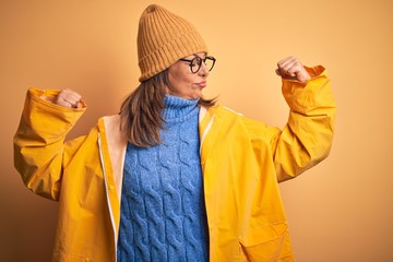 Sticker - Middle age woman wearing yellow raincoat and winter hat over isolated background showing arms muscles smiling proud. Fitness concept.