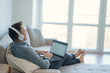 © Space_Cat - Man relaxing on sofa with laptop watching movie with headphones or working online