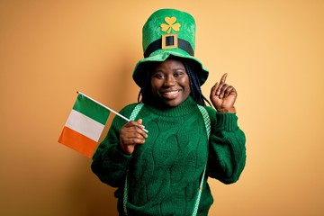 Plus size african american woman wearing green hat holding irish flag on saint patricks day surprised with an idea or question pointing finger with happy face, number one