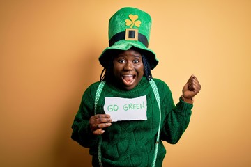 Plus size african american woman wearing green hat holding paper on saint patricks day screaming proud and celebrating victory and success very excited, cheering emotion