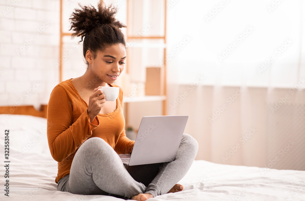 African American Lady Using Laptop Having Coffee Sitting On Bed - obrazy, fototapety, plakaty 