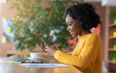 Wall Mural - Pretty afro girl drinking coffee and using smartphone