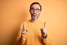 Middle Age Hoary Man Wearing Casual Sweater And Glasses Over Isolated Yellow Background Pointing Up Looking Sad And Upset, Indicating Direction With Fingers, Unhappy And Depressed.