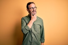 Middle Age Hoary Man Wearing Casual Green Shirt And Glasses Over Isolated Yellow Background With Hand On Chin Thinking About Question, Pensive Expression. Smiling With Thoughtful Face. Doubt Concept.