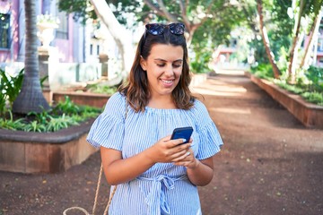 Wall Mural - Young beautiful woman smiling happy walking on city streets on a sunny day of summer using smartphone